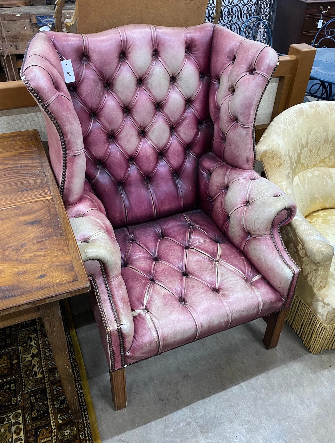 A George III style button back wing armchair upholstered in faded burgundy buttoned leather, width 82cm, depth 82cm, height 110cm